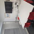 A photograph of meeting room 2. There is a white table with 6 chairs around it and a TV screen on the wall above the table. There is a framed picture next to the TV screen. The far wall is glass and the rest are white.