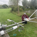 A man crouched down by the Thames River bank installing an eddy tower.