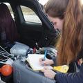 a woman leant over a field notebook and scientific equipment in the boot of a car