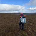 photo of a woman carrying river sampling equipment across a moorland