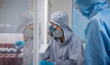 Photograph of two researchers in the clean suite. They are wearing protective gear and face masks.