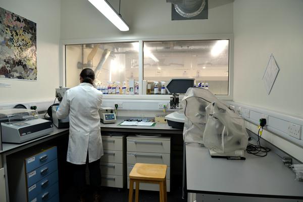 A view of the whole polishing lab. Two large polishing machines are visible in either corner, and lab manager Emily stands in a lab coat and gloves working on one.