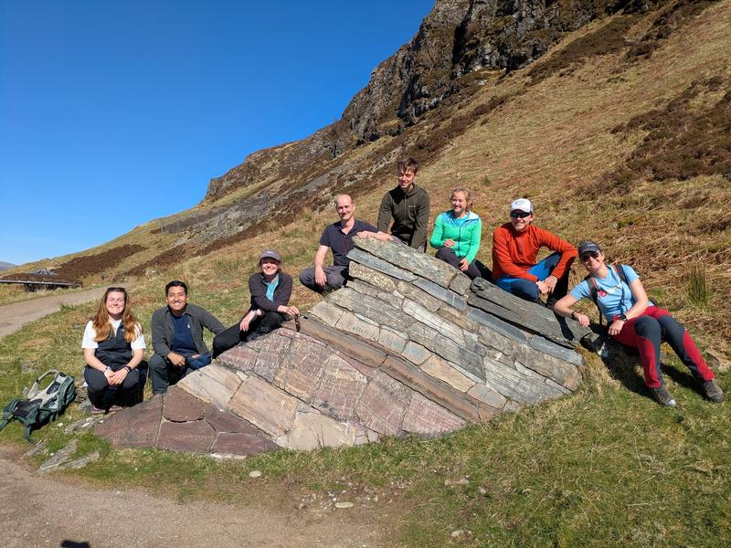 Photo of demonstrator team on the 2025 Assynt Fieldclass. A group of 8 people are sat on a large rock in the sunshine.