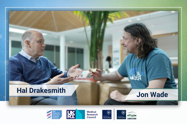 Jon and Hal in discussion, sat in a wide open atrium space. Jon is holding a scotch egg.