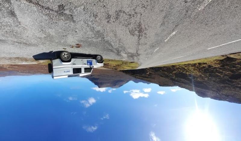 Photograph of the department landrover on the Assynt Field Class. The landrover is parked on a road overlooking a beautiful view with blue skies