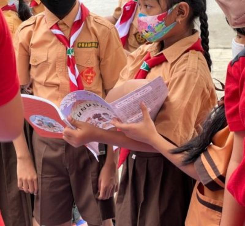 A group of children wearing an orange uniform reading the COPE volcano book