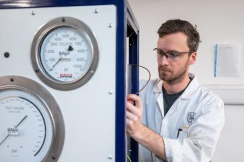 A man in a white lab coat adjusting a piston cylinder