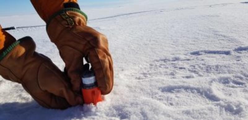 Seismic Node BAS A pair of gloved hands putting an orange node into the ice.