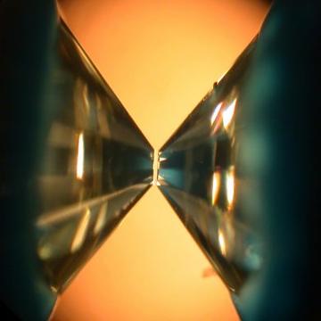 Zoomed in photograph of two crystals almost touching at their tips on a orange background