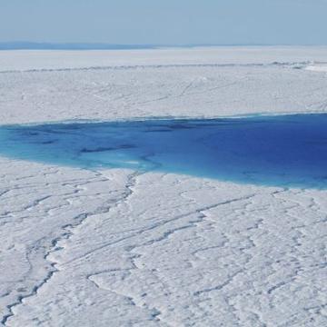 Image of an ice sheet with a bright blue lake in the middle of it 