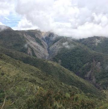 Peru Landslides Mountains in Peru covered in green vegetation, a landslide is occurring in the background down one of the mountains, there are lots of clouds in the sky.