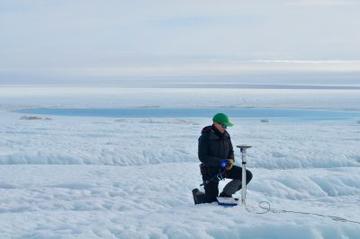 Laura Stevens kneeling down on the middle of an expanse of ice working with an instrument.