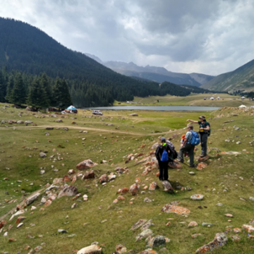 Three people standing in a grassy valley between some vegetation covered mountains 