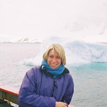 An image of Ros on a boat, leaning against the deck rail. Behind her is the ocean and mutliple white icebergs