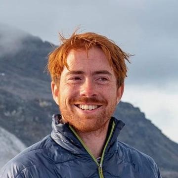 A headshot of Ross Anderson with some foggy mountains in the background.