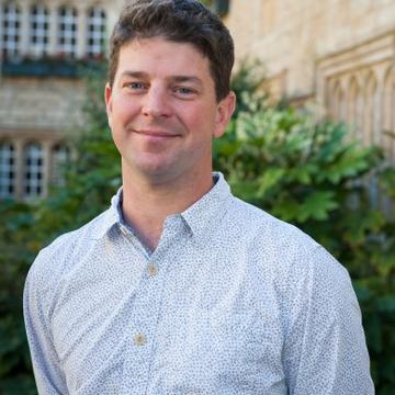 A headshot of Stuart standing in front of a tree and an old building in the Teddy Hall front quad