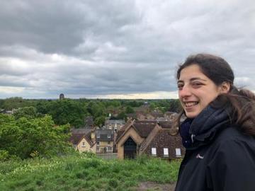 A photo of Hannah on a hill with a view over some trees and a village