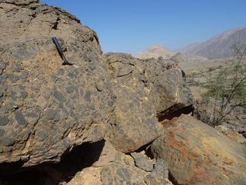 Hendrik Photo A photo of some rocks with a hammer on them for scale in a dry basin, you can see mountains in the background