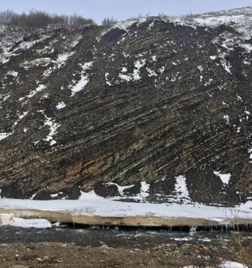 Shale Rocks, Canada A dark brown cliff covered on the top with snow. Along the cliff you can see diagonal lines in the rock showing beds.