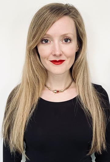 Erin Saupe Head and shoulder photograph of Erin Saupe. She has long blonde hair and is wearing a black top. She is wearing red lipstick and smiling at the camera.