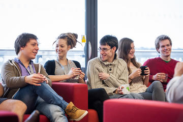 Common Room Photograph of a group of researchers sat on red sofas in the common room laughing and talking.