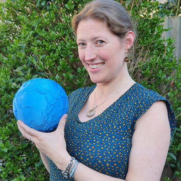 A headshot of Paula in front of a hedge holding a blue model of a globe.