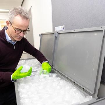Gideon Henderson examining a sample in a lab, leaning on a large trunk of samples