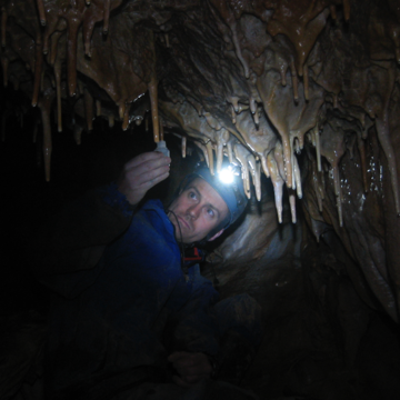 Gideon Henderson working in a cave, looking at a stalagmite with a headtorch on