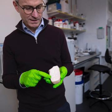 Gideon Henderson holding a slice of a stalagmite in a laboratory