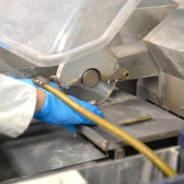 A gloved hand holds a sample being cut by a trim saw