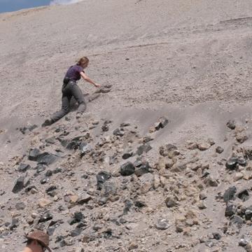 Volcanology Group Photograph of a researcher working on the side of a volcano. The ground is light brown and looks sandy.