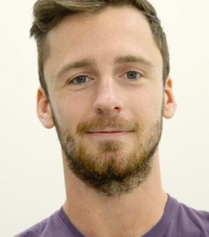 Passport-style photograph of James King. He has short hair and a beard and is wearing a purple tshirt.